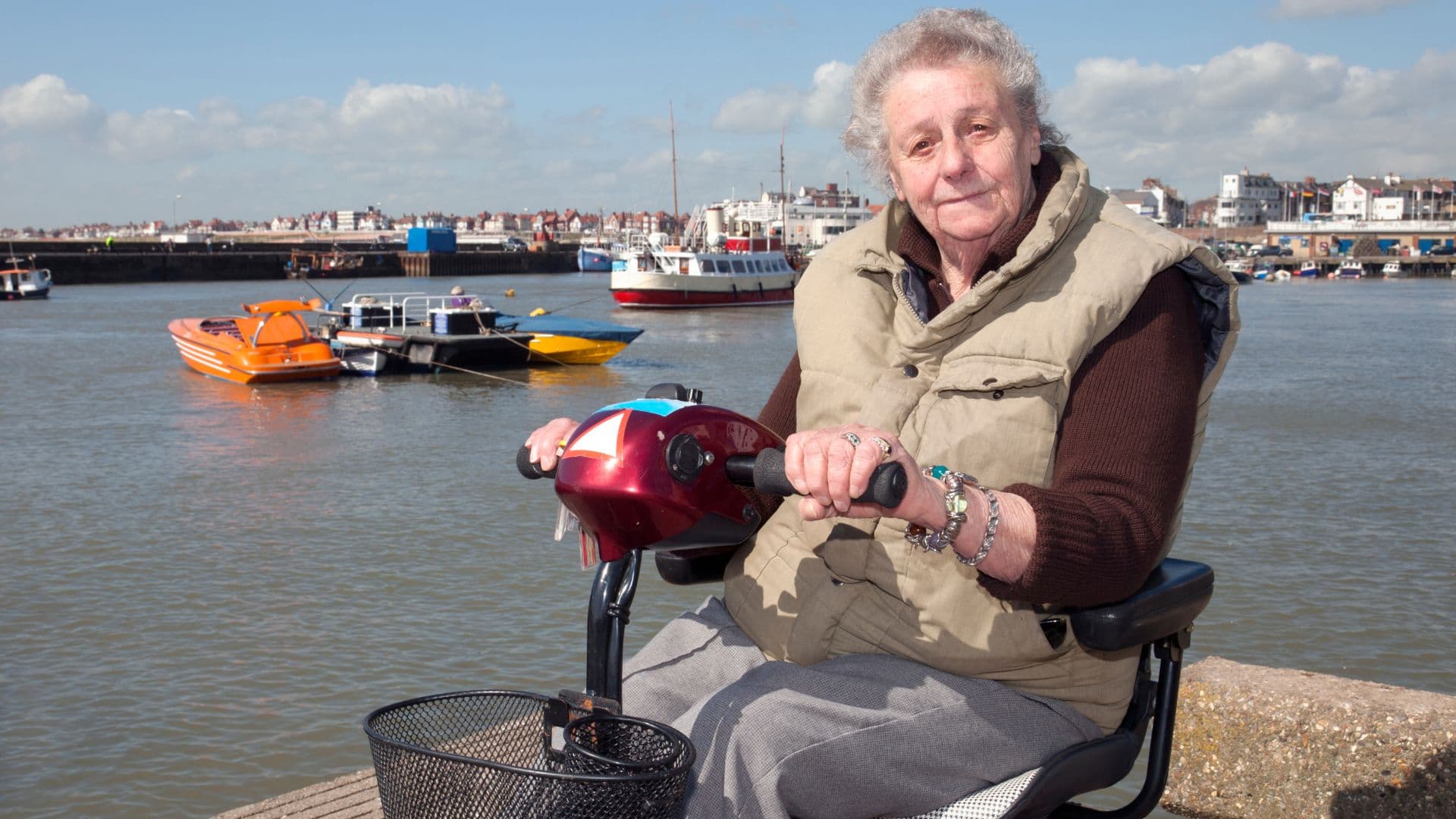 A man on a mobility scooter beside a harbour