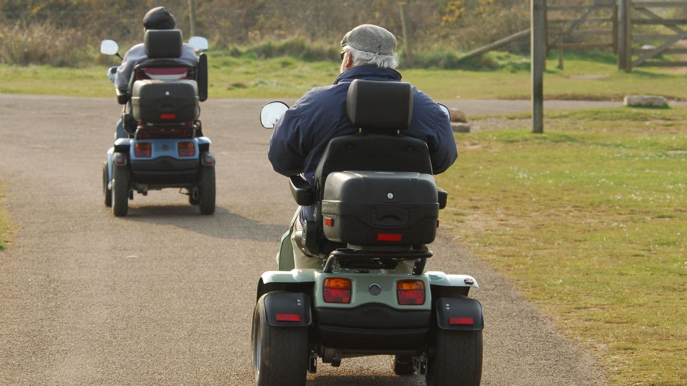 Two people riding mobility scooters side by side through a park